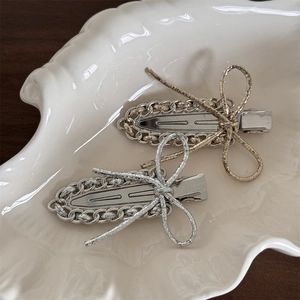 Detailed close-up of gold and silver metal bow hair clips with chain design on a shell plate
