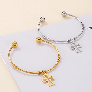 Detail of cross charm on gold and silver stainless steel open bangles with ball ends