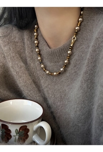Gros plan du collier perles dorées et pierres œil de tigre sur un pull marron élégant