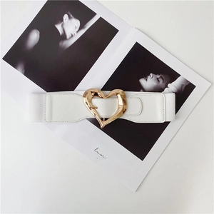Detail of white elastic waist belt with a polished gold heart buckle on a magazine