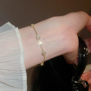 Close-up of gold chain bracelet with green zircon and pearl details on a model's wrist