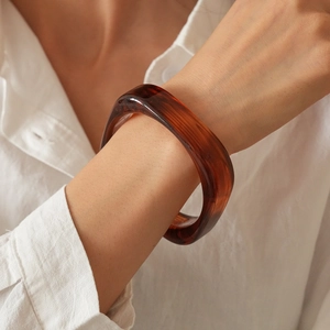Close-up of a wide geometric resin bangle in dark brown on a model's wrist