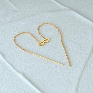 Artistic layout of gold heart drop threader earrings on a textured white surface