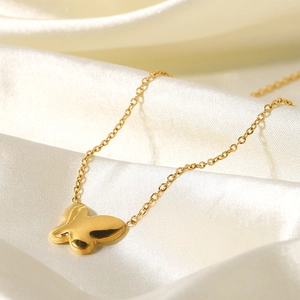 Close-up of gold butterfly pendant on white silk fabric with elegant metal texture