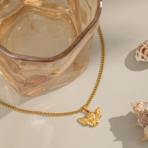 Élégant collier ange doré en acier titane sur un fond beige chaud et naturel