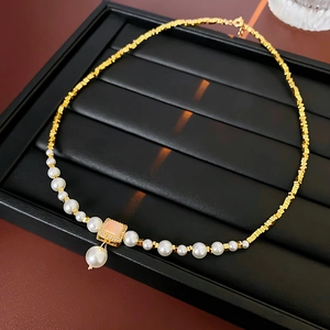 Detail of 18k gold plated necklace with pink square gem and pearl drop on black tray