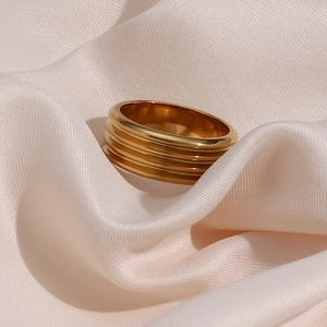 Detailed view of an 18K gold-plated ribbed ring on an elegant beige silk fabric background