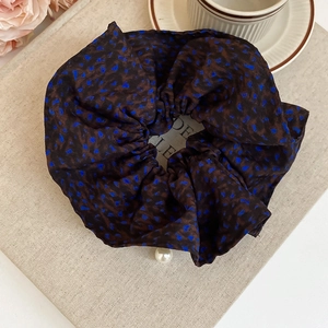 Close-up of leopard print fabric scrunchie with a white pearl charm on a book