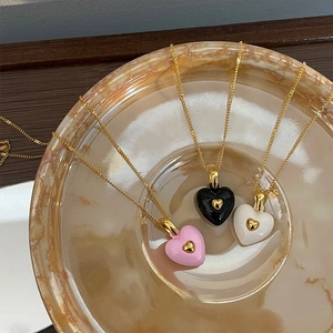 Detailed view of vintage enamel heart necklaces in pink, black and white with gold chains