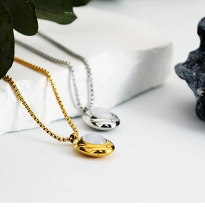 Macro shot of oval shell pendants in gold and silver finish with elegant box chains