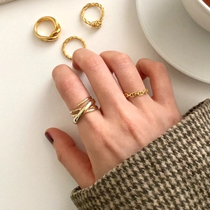 Close-up of a stacked gold woven ring set on fingers next to a coffee cup