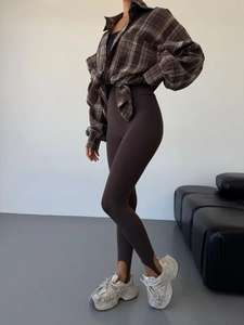 Detail of high-waisted stirrup yoga pants in dark coffee with retro plaid shirt and sneakers