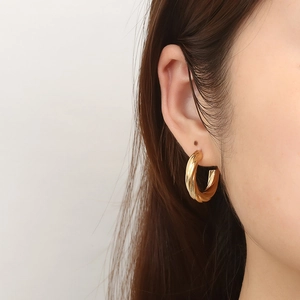 Boucle d'oreille créole torsadée en acier inoxydable doré 18K portée par un modèle