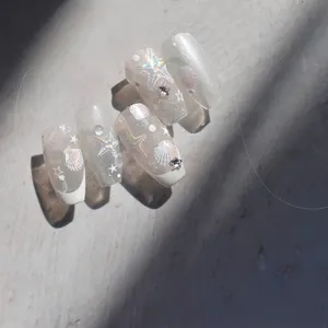 Detail of silver cat-eye nails with white French tips, shells and metallic stars