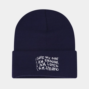 Detail of navy blue beanie featuring white I AM ENOUGH embroidery and knit texture