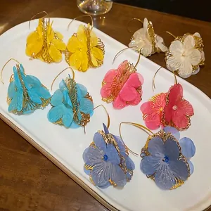 Cinq paires de créoles florales de couleurs variées sur un plateau en céramique