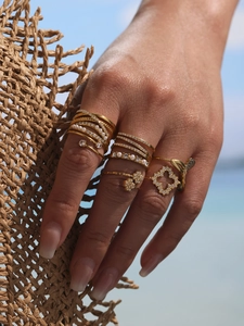 Close-up of gold geometric zircon rings with pearls on hand at a sunny beach setting