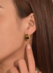 Close-up of a model wearing round tiger eye stud earrings with a gold-plated frame