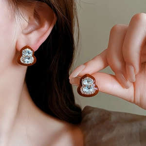 Close-up of brown enamel gourd earrings with sparkling rhinestones on ear and held by hand