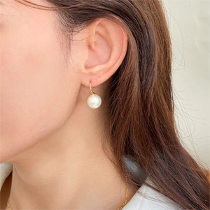 Close-up of elegant white pearl drop earring with gold hook on a model's ear