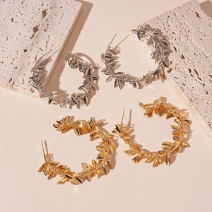 Golden and silver metal hoop earrings with delicate leaf design on travertine stone