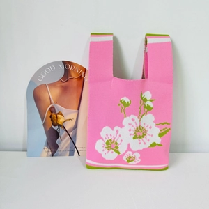 Detail of pink knitted tote bag with white floral pattern and green handles