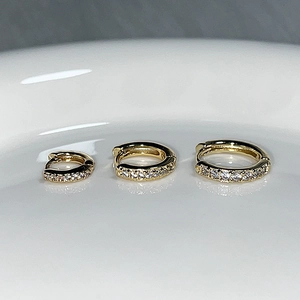 Detailed close-up of three sparkling gold hoop earrings with small diamonds on ceramic
