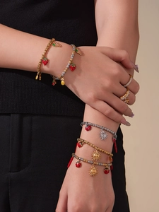 Detail of layered gold beaded bracelets with colorful enamel strawberry and pineapple charms