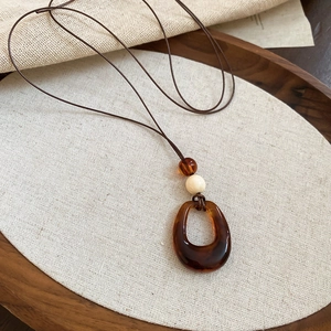 Détail d'un pendentif étoile en résine ambrée avec perle en bois sur cordon ciré marron