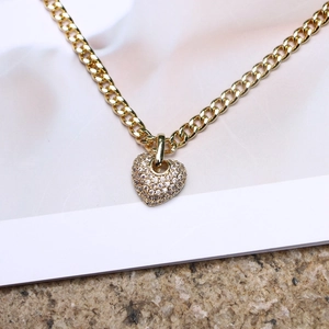Detail view of a gold heart pendant with micro-pave zircons on a cuban link chain