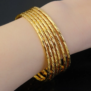 Detail of six gold plated 3mm bangles with diamond-cut texture on a woman's wrist