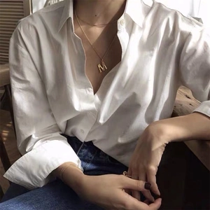 Détail d'un collier lettre M doré 14K avec texture bambou porté sur une chemise blanche chic