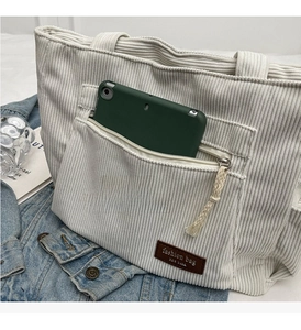 Detail of corduroy tote bag featuring a front zip pocket with a green tablet inside