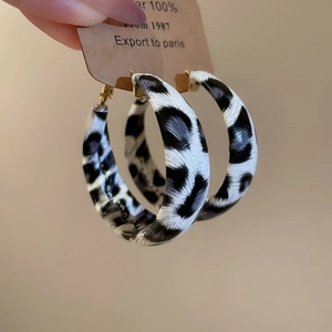 Detail view of large gold-clasp hoop earrings featuring a black and white patterned resin finish