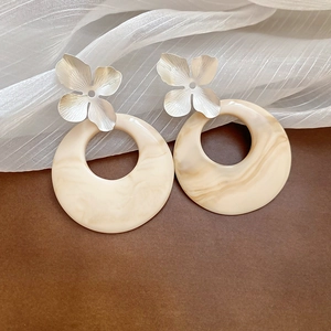 Detail of silver flower studs and creamy marble resin rings with fine brushed texture