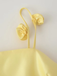 Close-up of yellow satin dress featuring delicate straps and elegant 3D knot detail