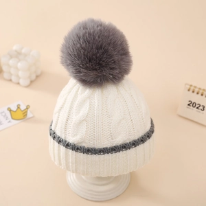 Close-up of baby knit hat showing soft cream cotton texture and grey faux fur pompom