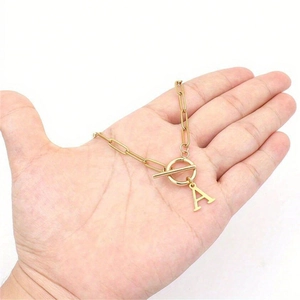 Detailed shot of golden paperclip chain necklace with sparkling letter A and OT clasp toggle