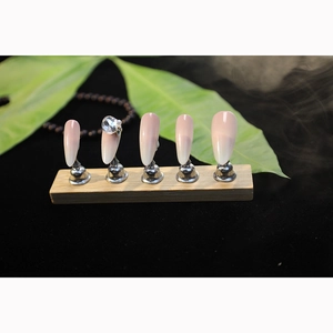 Nude gradient press-on nails with large rhinestone accent on professional display stand