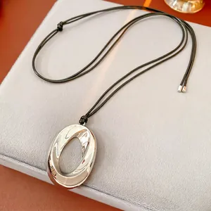 Minimalist silver oval hollow pendant necklace with black cord on gray velvet display