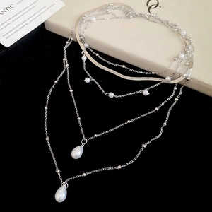 Macro shot of silver-colored layered necklace with waterdrop pearls and snake chain