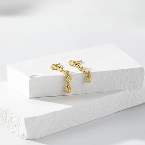 Detailed close-up of golden irregular pebble-shaped tassel earrings on white stone pedestals
