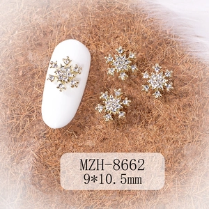 Macro detail of gold snowflake nail charms with rhinestones on a white nail tip display