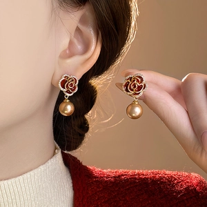 Detailed close-up of a red enamel rose earring with gold edges and a large golden pearl drop