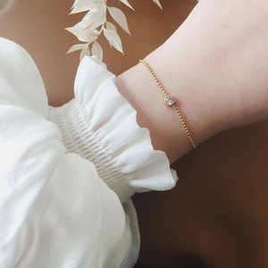 Élégant bracelet en perles plaqué or 18K avec zircon blanc solitaire au poignet d'une femme