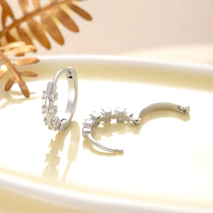 Elegant silver circle earrings with inlaid zircons on a ceramic plate with golden leaf decor
