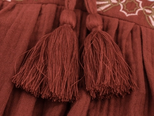 Close-up of geometric embroidery and dual tassels on textured brick red fabric detail