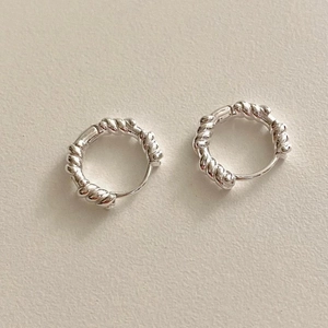 Detailed macro view of S925 sterling silver twisted rope hoop earrings on beige background