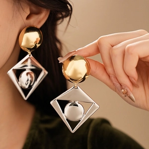 Statement geometric earrings featuring gold disc and silver diamond frame on a model