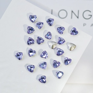 Macro detail of purple heart-shaped K9 crystal nail art rhinestones with silver backing